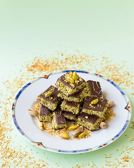 a stack of chocolate topped pistachio bars on a decorative plate