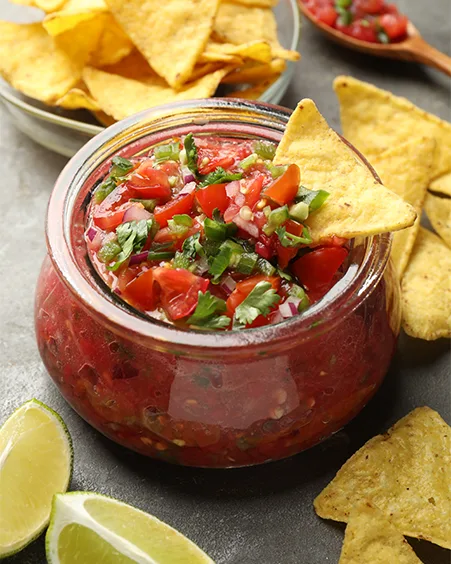 salsa in jar lime and nachos on grey table closeup